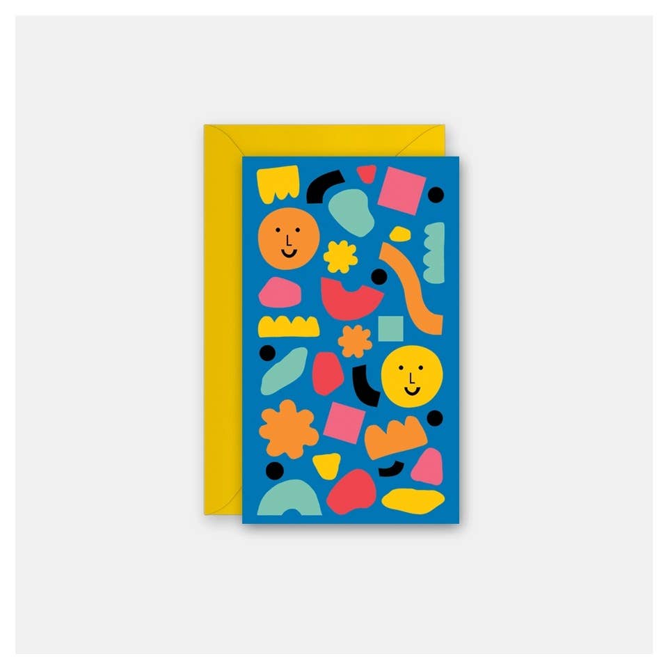 A greeting card with a bright blue background covered in colorful abstract shapes and smiley faces, shown with a yellow envelope behind it on a light gray background.