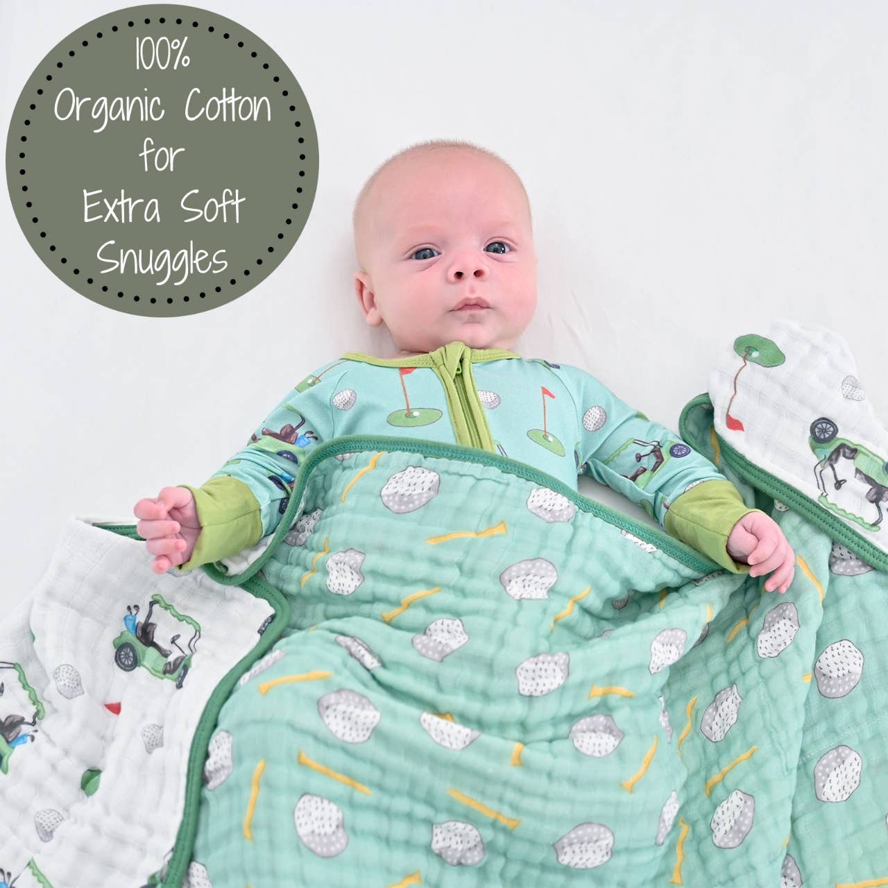 A baby is laying on a white surface wearing golf-themed pajamas and has a muslin quilt with a green trim and a golf theme, featuring various golf-related graphics covering the baby's clothing from the waist down.