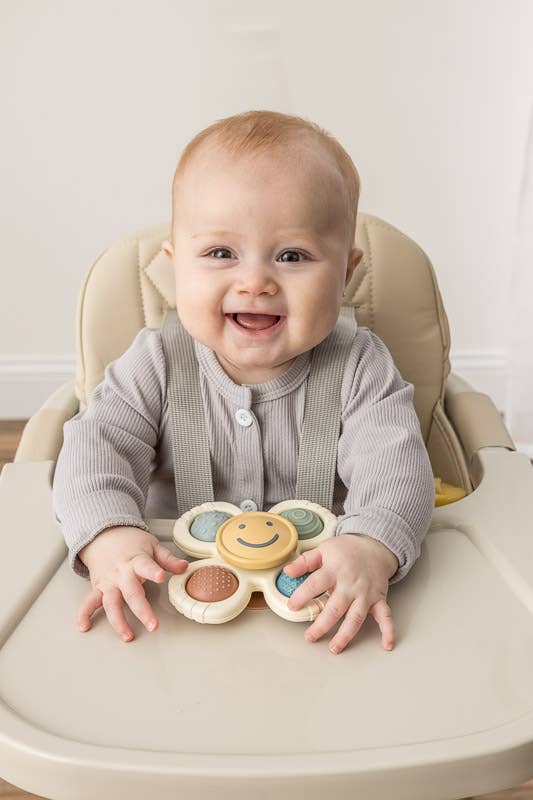 Smiling baby in a high chair with a spin toy on the table top.