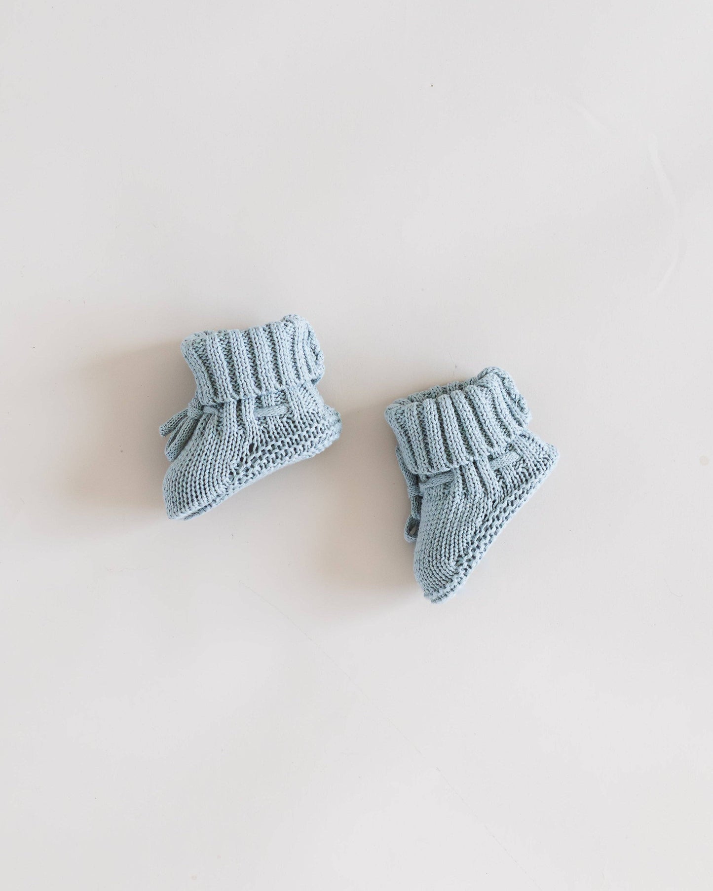 Pair of blue knitted baby booties on a light beige background