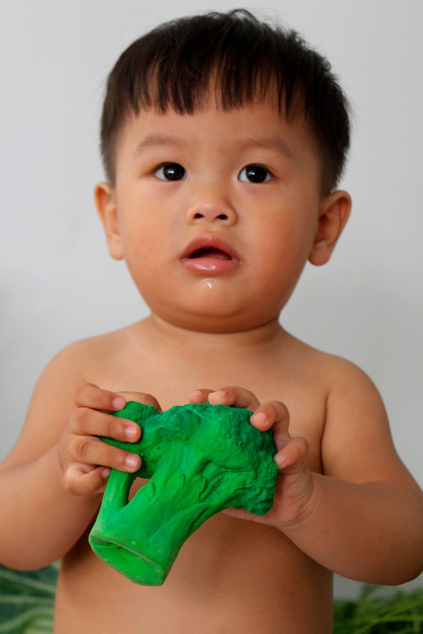 Child holding a green teether broccoli against a plain background