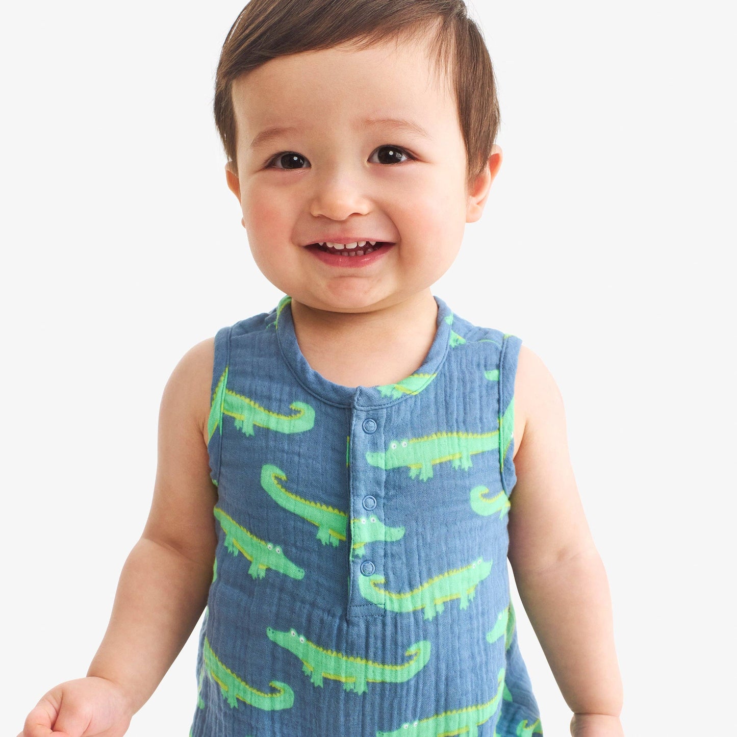 Child wearing a blue sleeveless shirt with green alligator patterns on a white background