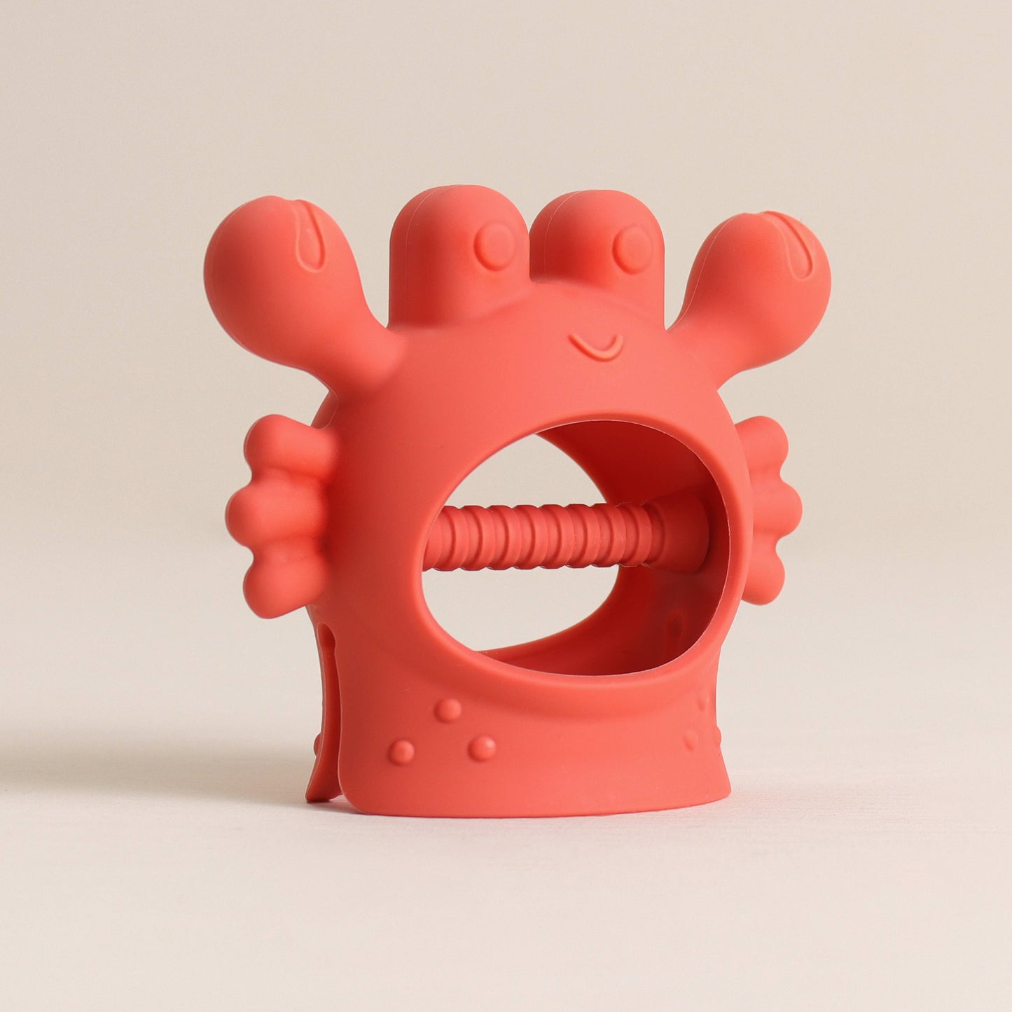 Red silicone teething ring with a smiling face on a beige background
