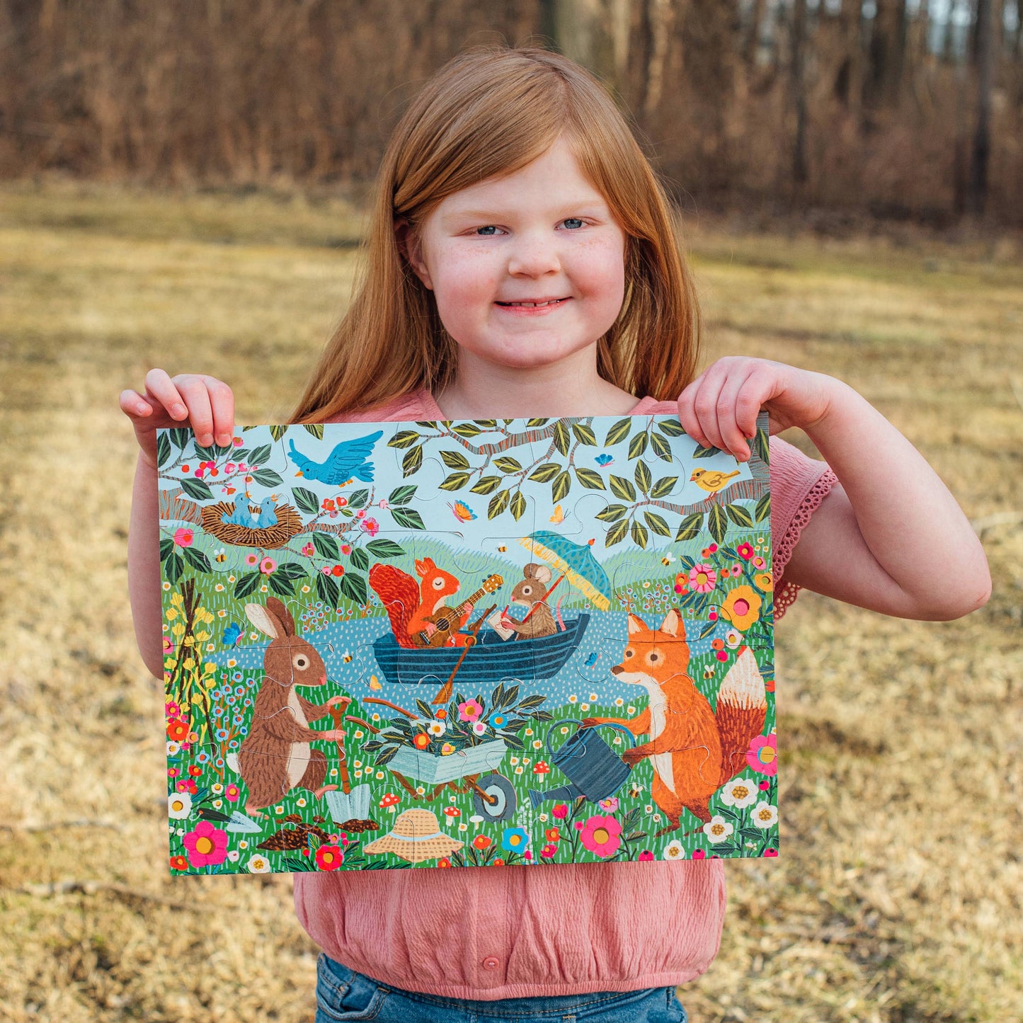 Young girl holding a colorful forest-themed fabric panel outdoors.