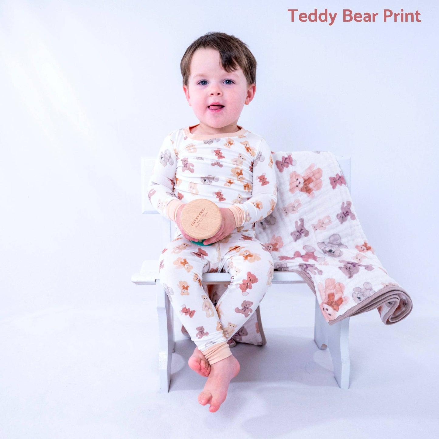 Child wearing teddy bear print pajamas sitting on a chair with a matching blanket.