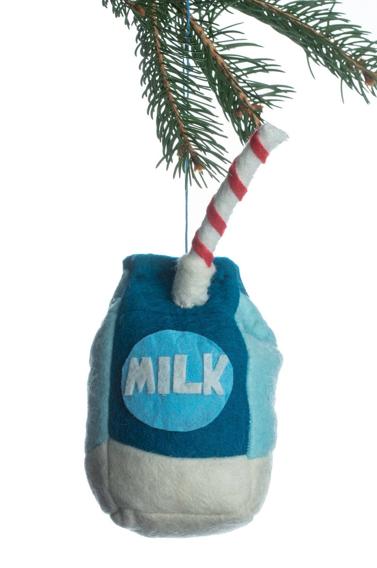 A plush milk bottle Christmas ornament hanging from a pine branch, featuring a blue body, white base, a red-and-white striped straw, and the word 'MILK' on the front.
