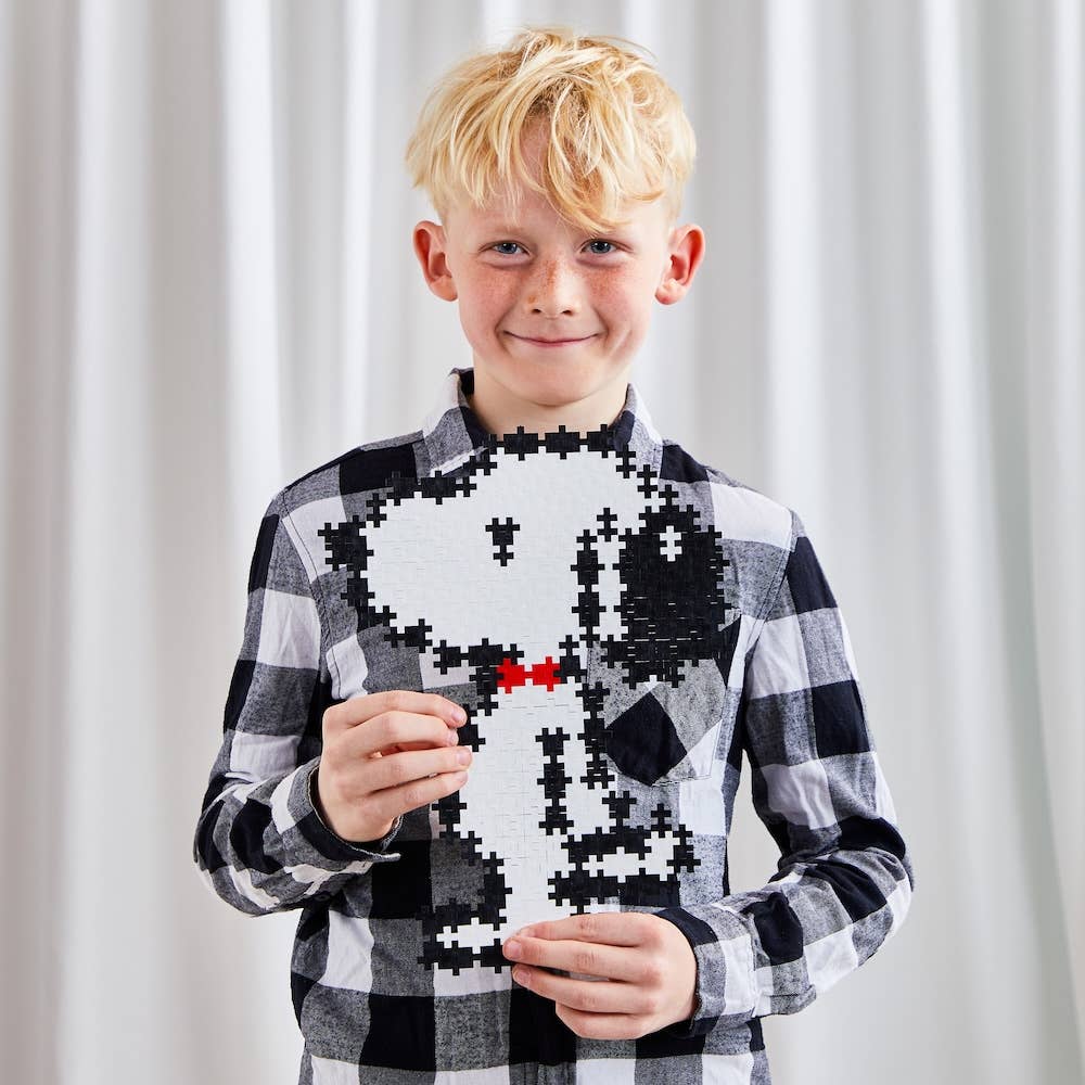 Child wearing a black and white checkered shirt with a pixelated Snoopy puzzle design, standing against a plain background.