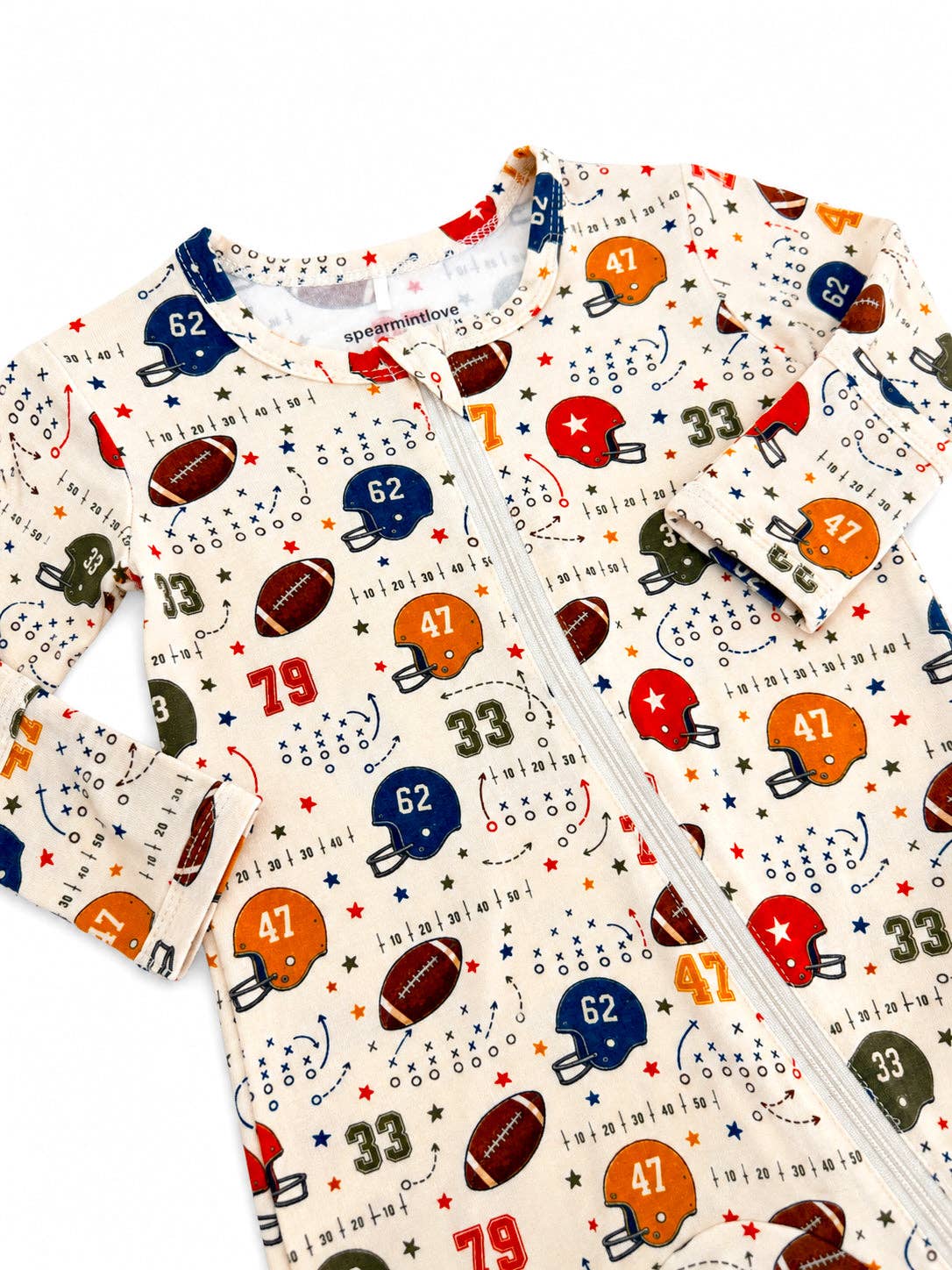 A baby long-sleeve zip-up romper with an all-over football print on a cream background. The pattern features various football helmets in blue, orange, red, and green, along with footballs, numbers, and track-and-field graphics.