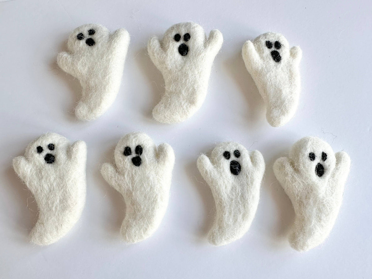 Seven white felt ghosts with black eyes and mouths, arranged on a plain white background.