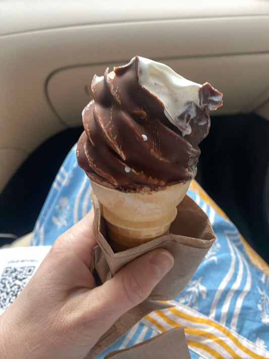 White hand holding an ice cream cone covered in chocolate shell. 