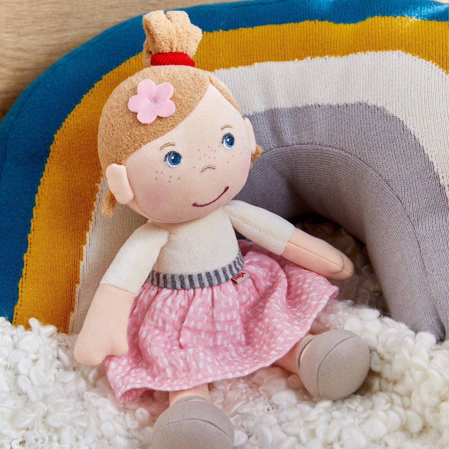 Plush doll with a pink dress and flower headband on a colorful background