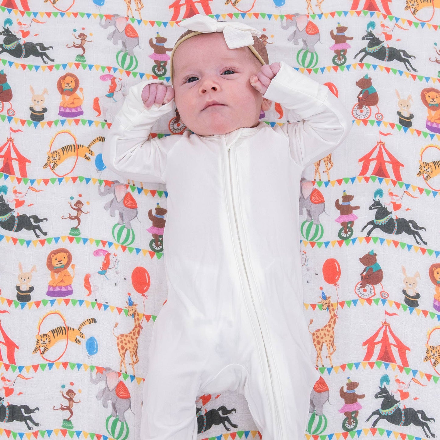 Baby lying on a colorful patterned swaddle blanket with animal illustrations