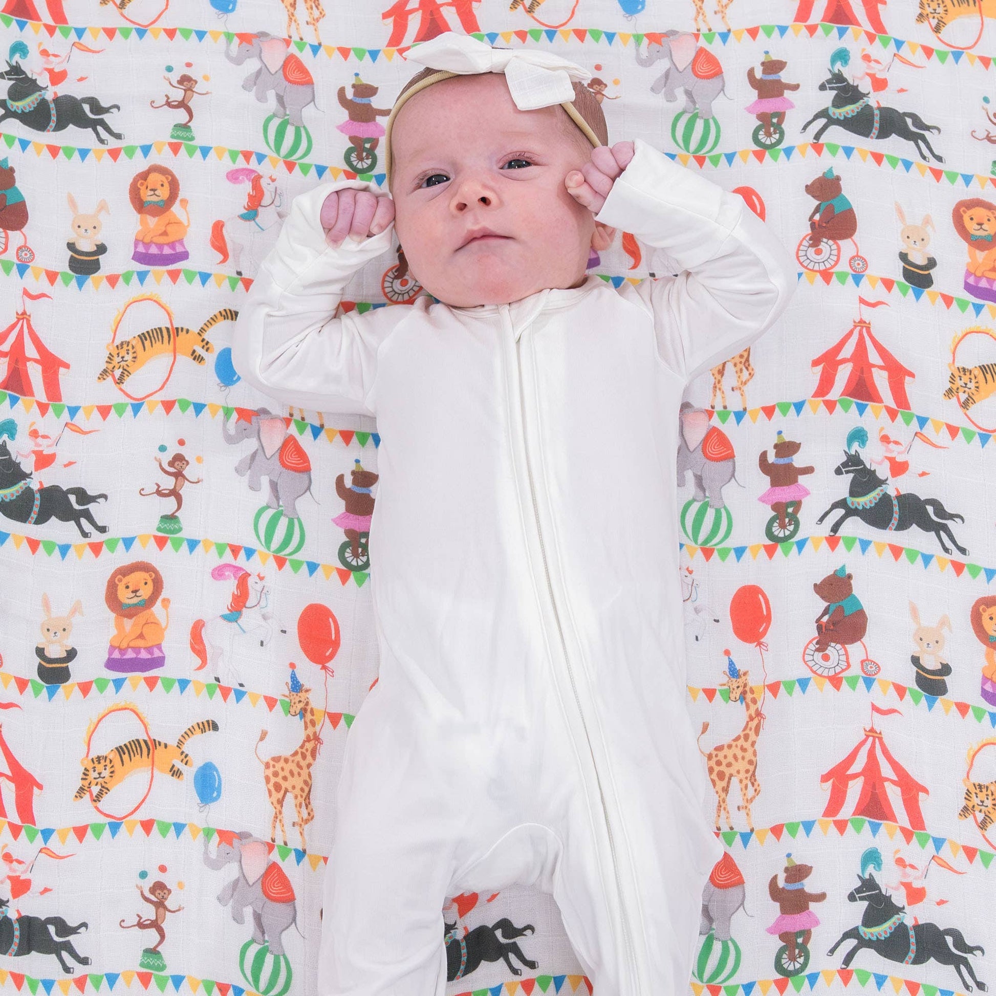 Baby lying on a colorful patterned swaddle blanket with animal illustrations