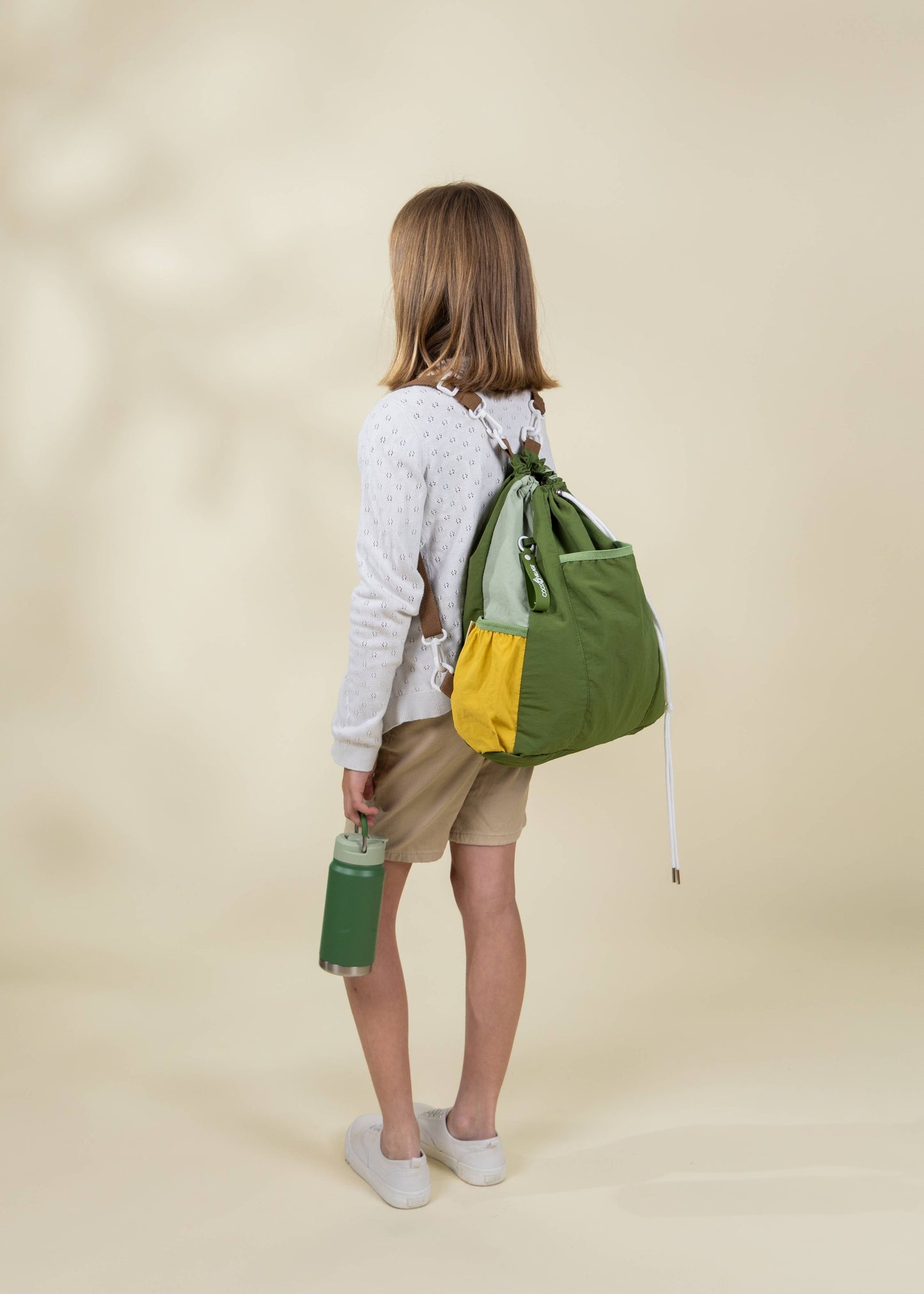 Person wearing a green and yellow backpack on a beige background