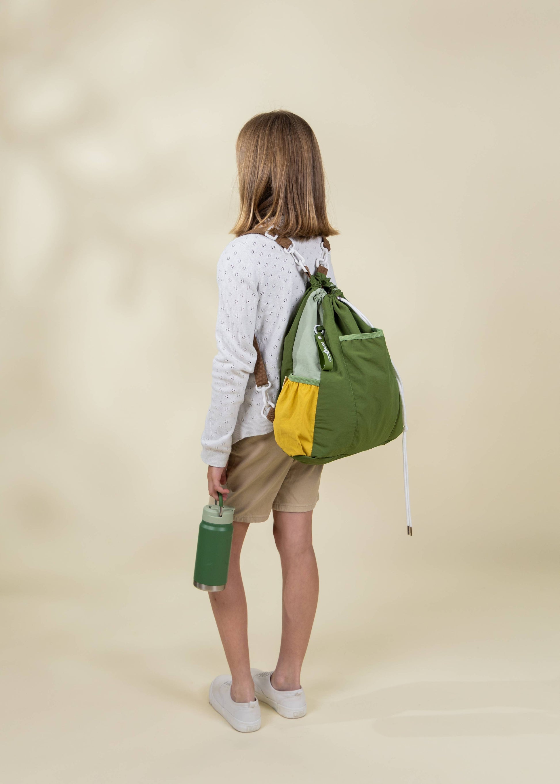 Person wearing a green and yellow backpack on a beige background