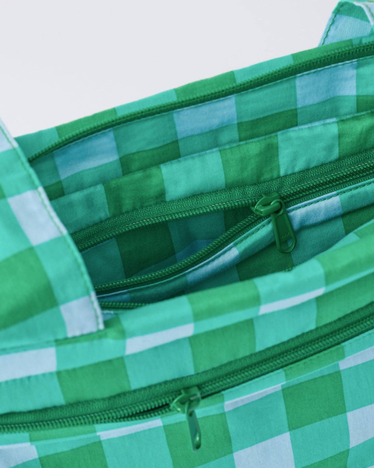 Close-up of a green and white checkered bag showing the interior lining, a zippered pocket, and green zipper pulls.