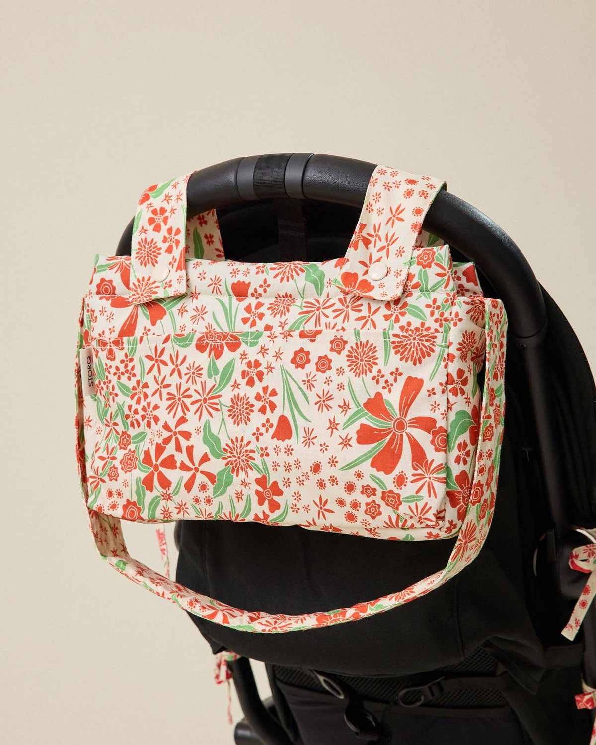 Floral-patterned baby carrier with red and green flowers on a beige background
