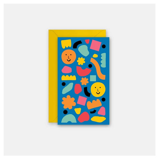 A greeting card with a bright blue background covered in colorful abstract shapes and smiley faces, shown with a yellow envelope behind it on a light gray background.