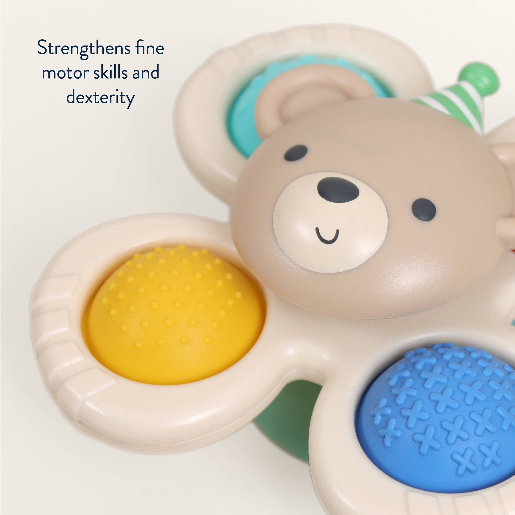 A close-up of a bear-shaped sensory toy with three textured buttons in yellow, blue, and green, on a white background with text that reads 'Strengthens fine motor skills and dexterity'.