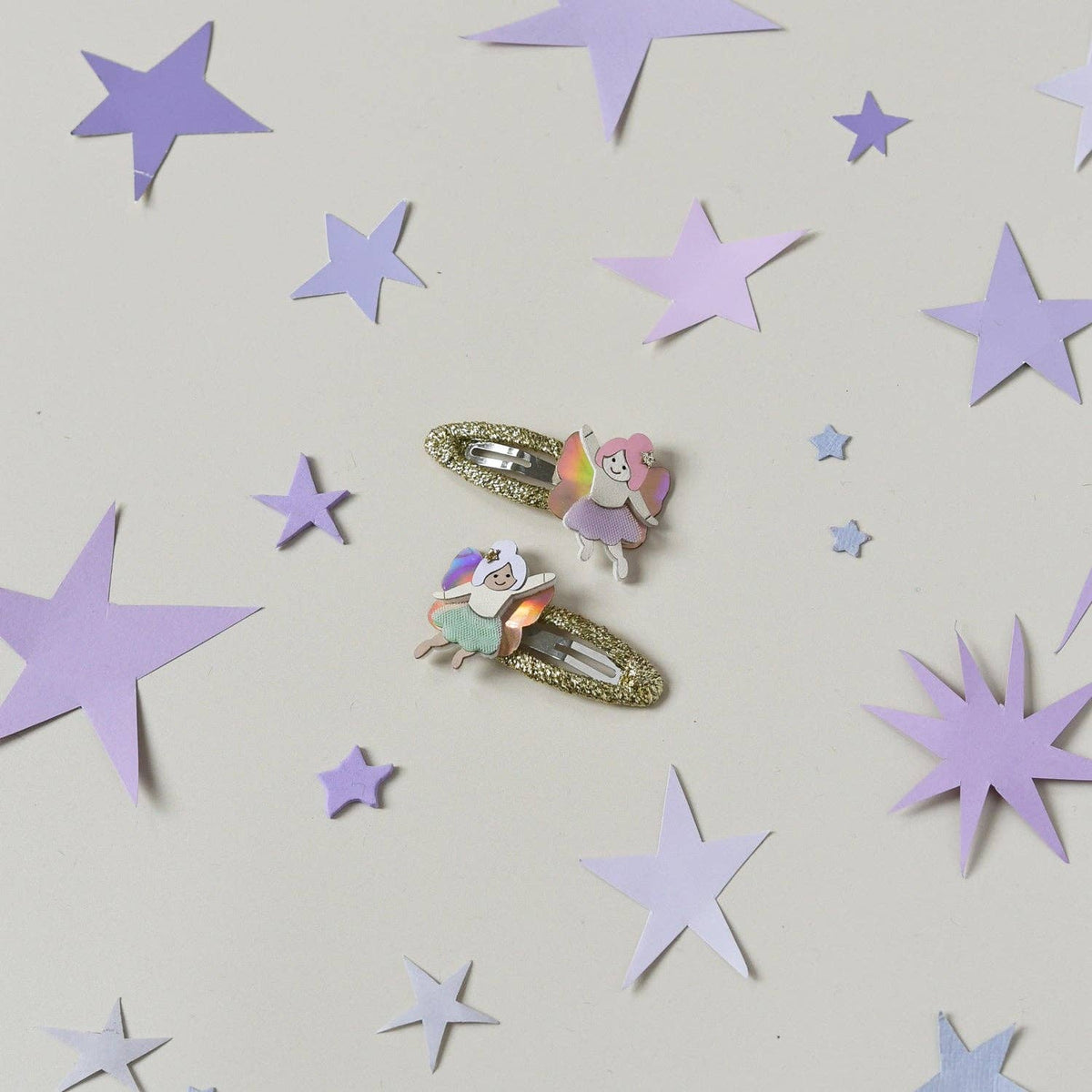 Two hair clips with fairy designs on a light gray background with purple stars.