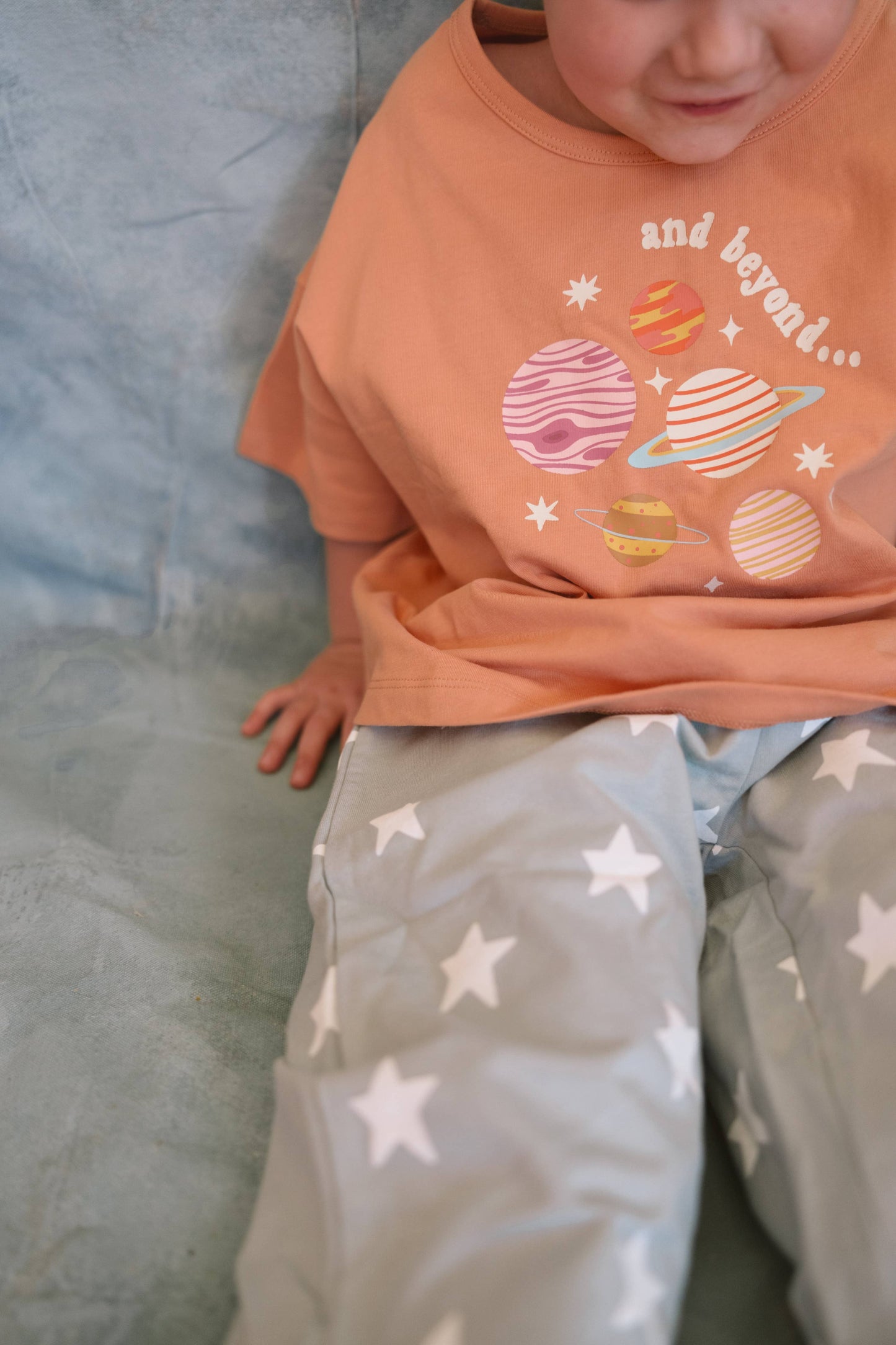 Child wearing an orange t-shirt with space-themed graphics and gray pants with star patterns.