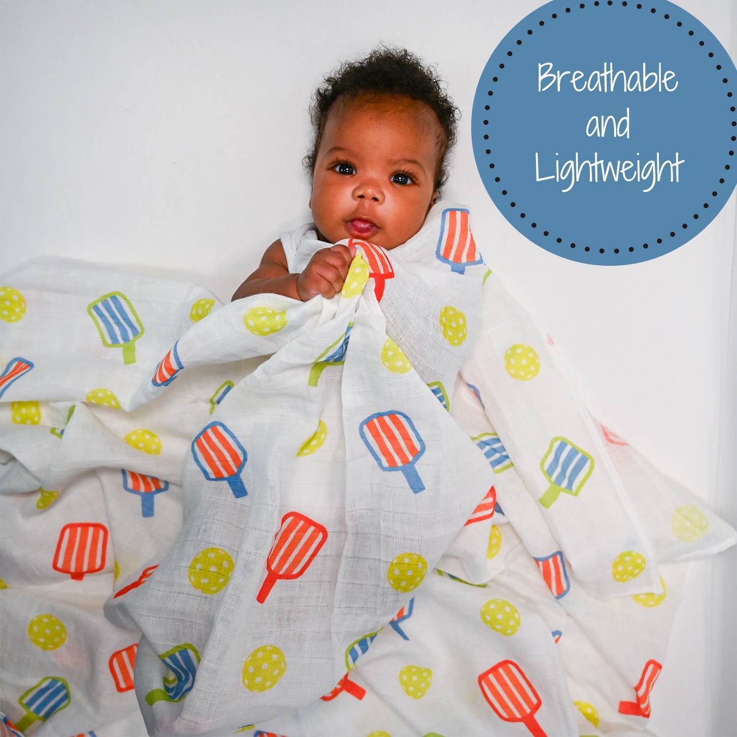 Baby wrapped in a colorful blanket with a pickleball pattern on a white background.