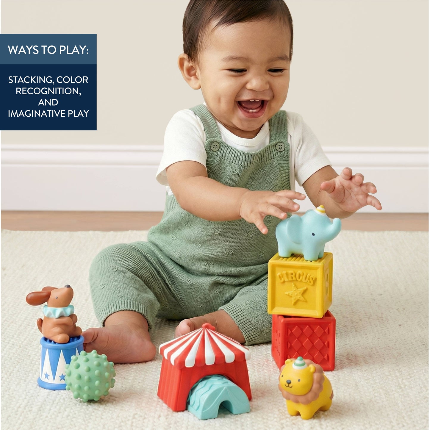 A baby sitting on a light beige carpet plays with colorful circus-themed  blocks and animal toys. The baby wears a white t-shirt and a sage green knit overalls.