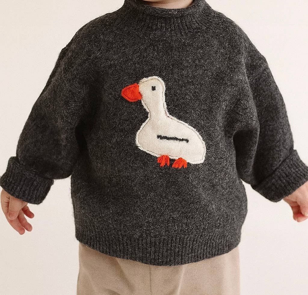 Child wearing a dark gray sweater with a white duck design on a plain background