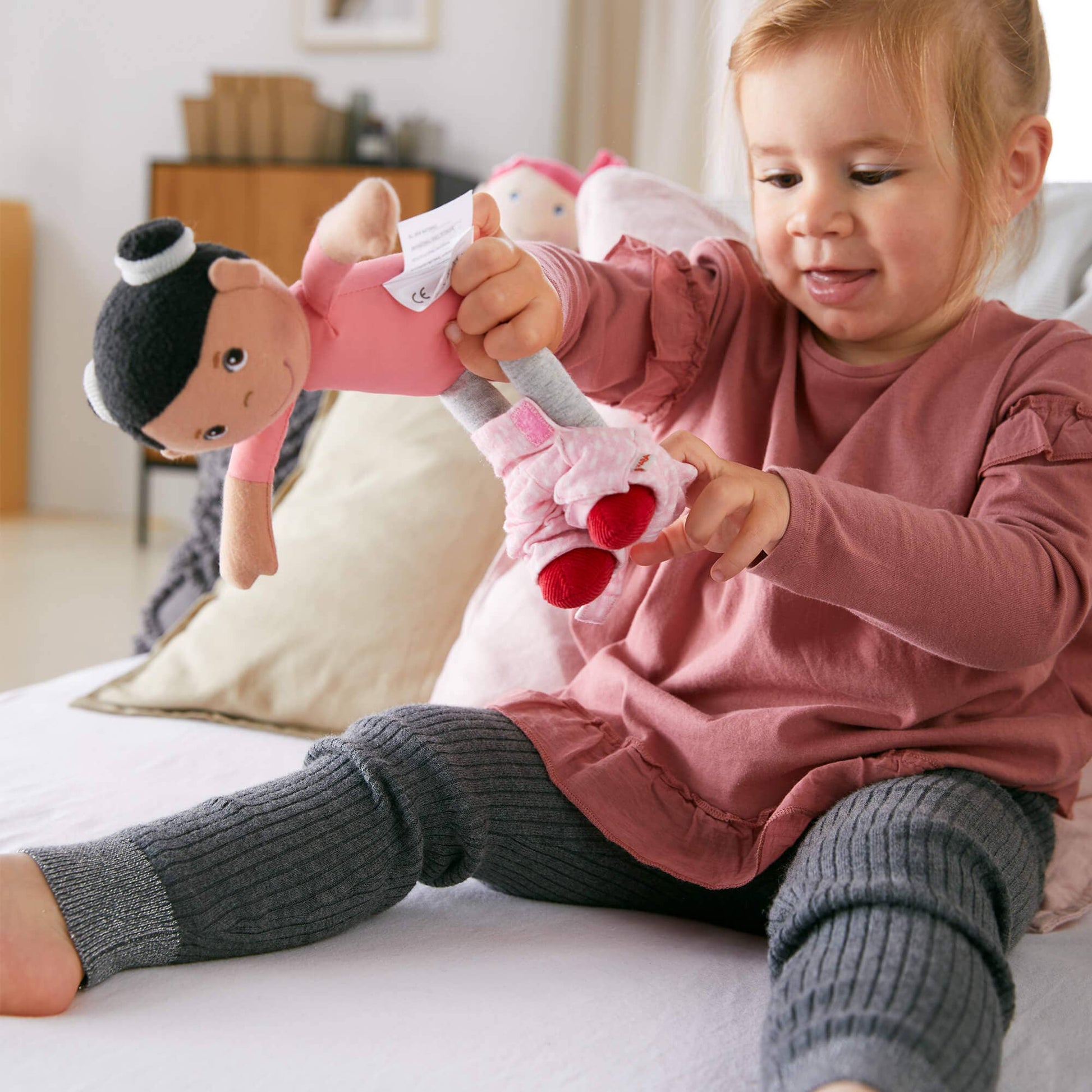 Child playing with a plush toy on a bed in a bedroom setting