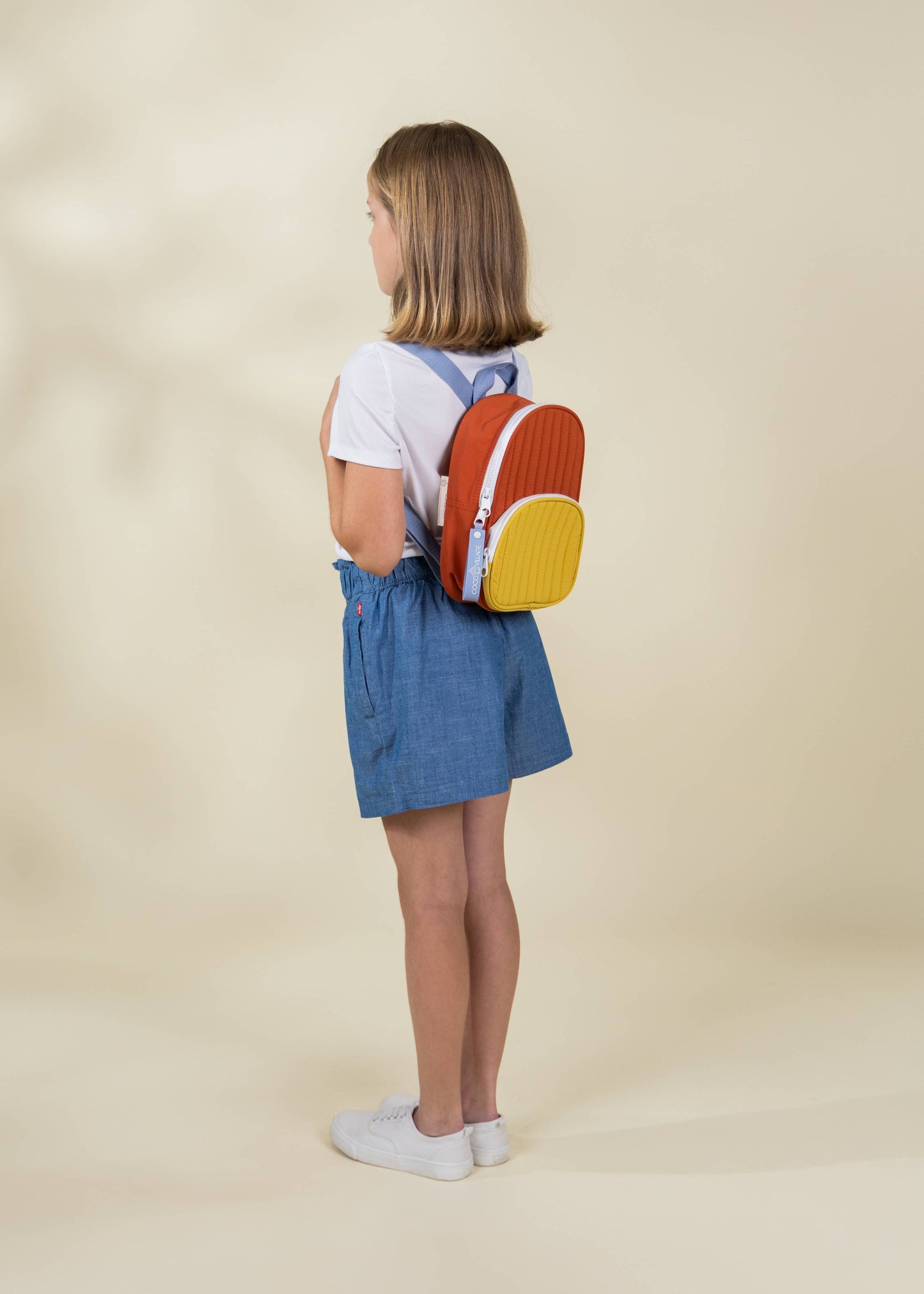 Child wearing a colorful backpack on a beige background