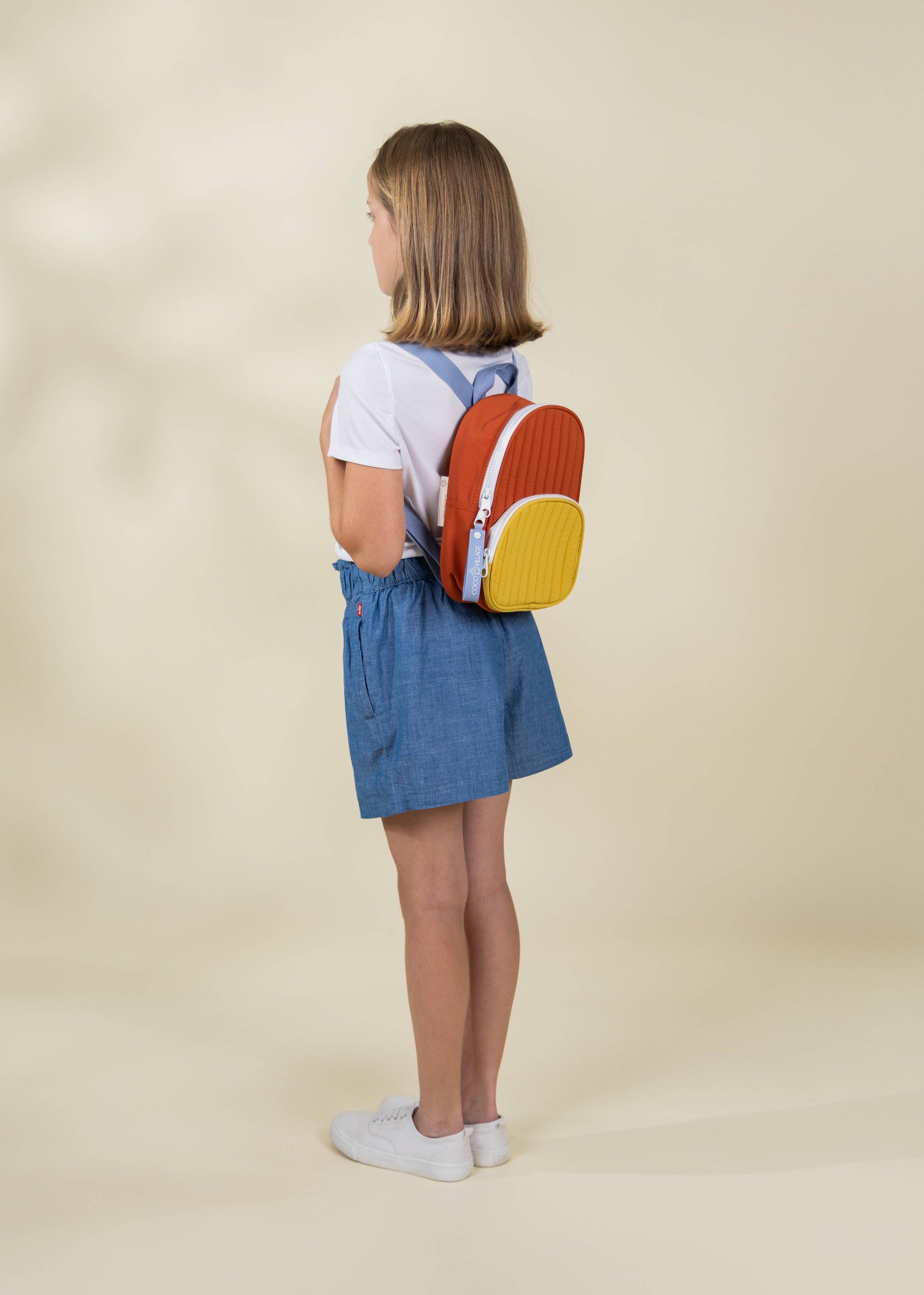 Child wearing a colorful backpack on a beige background