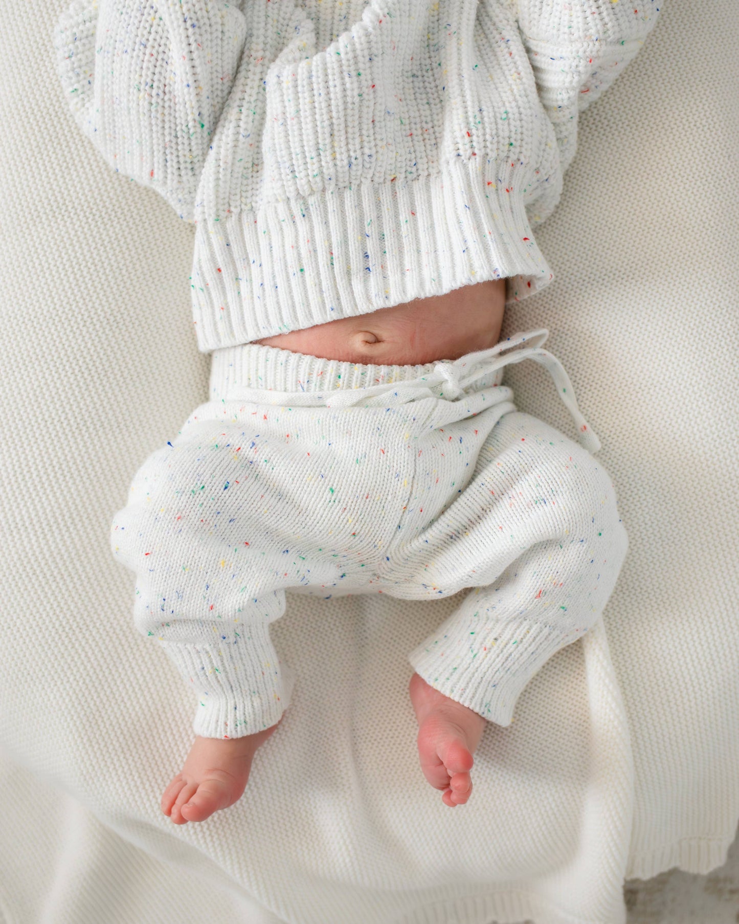 Baby wearing a white knitted outfit on a neutral background