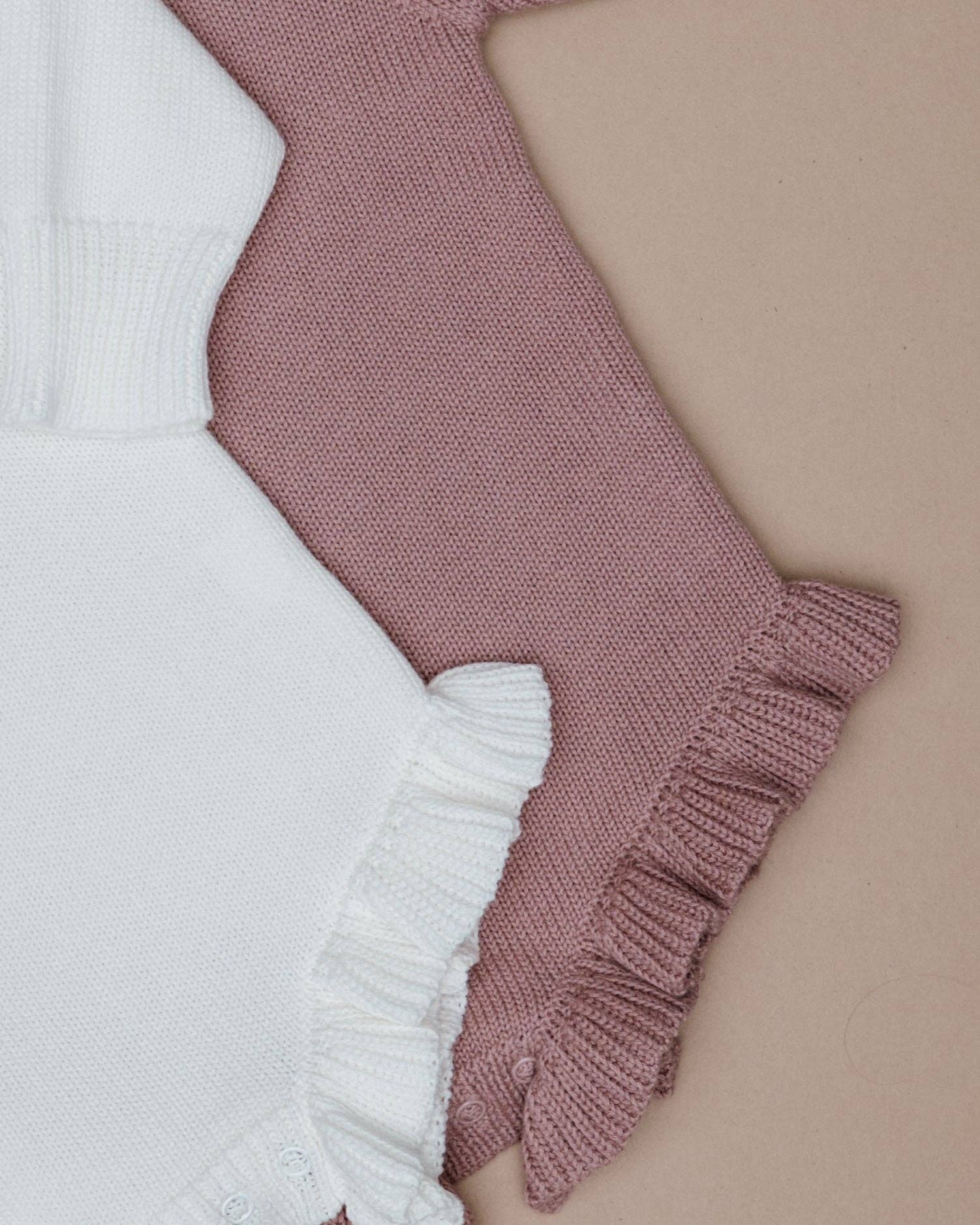 Knitted baby romper with white and pink ruffled design on a beige background