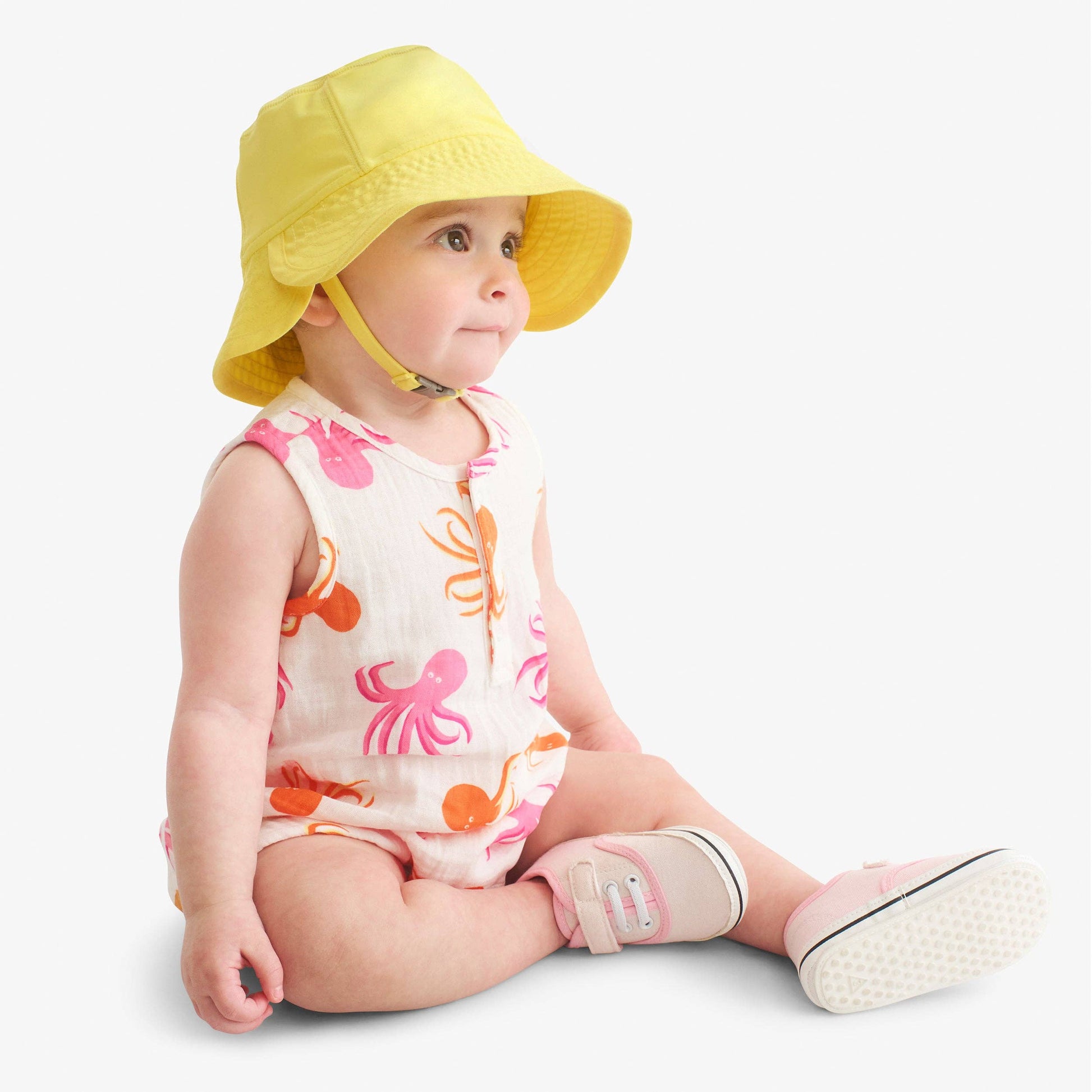 Baby wearing a yellow sun hat and colorful outfit on a light gray background