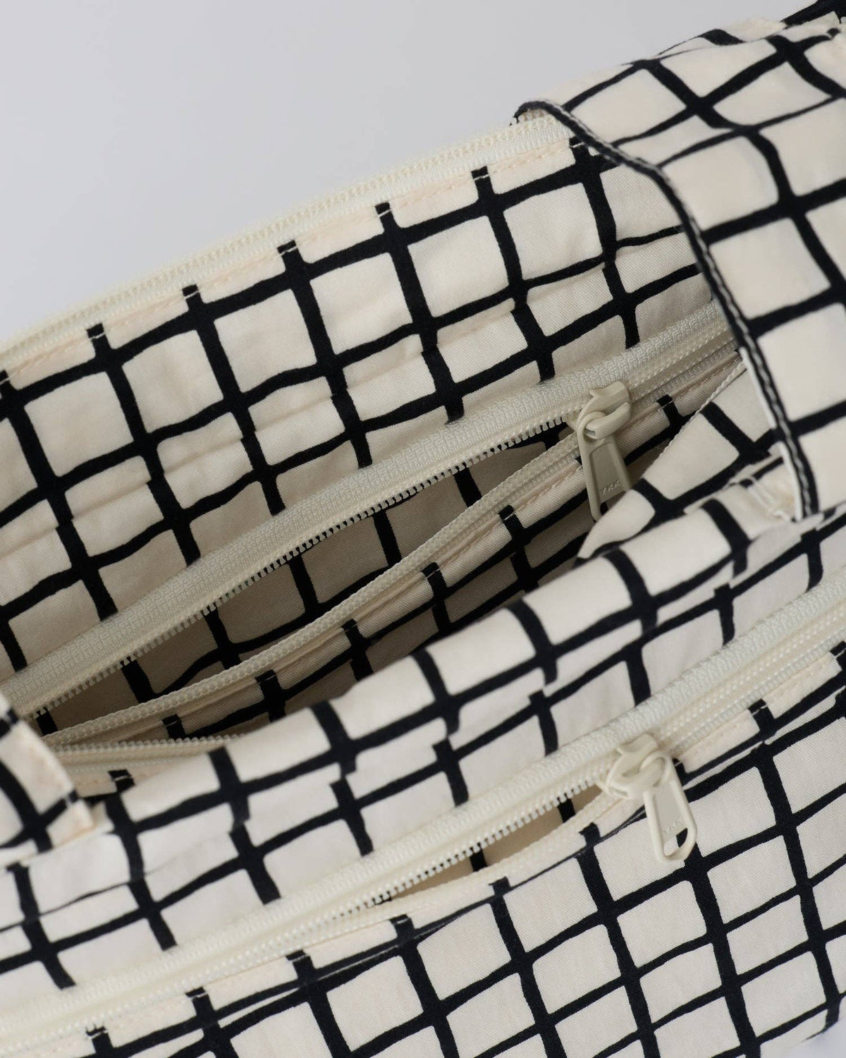 Close-up of a black and off-white grid patterned bag with multiple zippered compartments.
