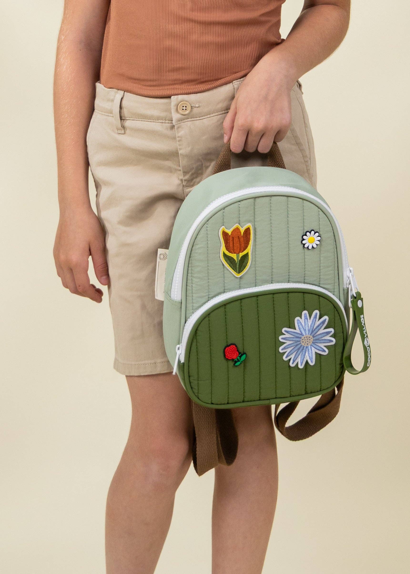 Green backpack with floral designs held by a person on a beige background