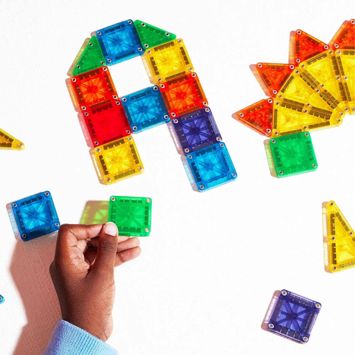 Colorful magnetic building blocks on a white background with a hand holding one block.