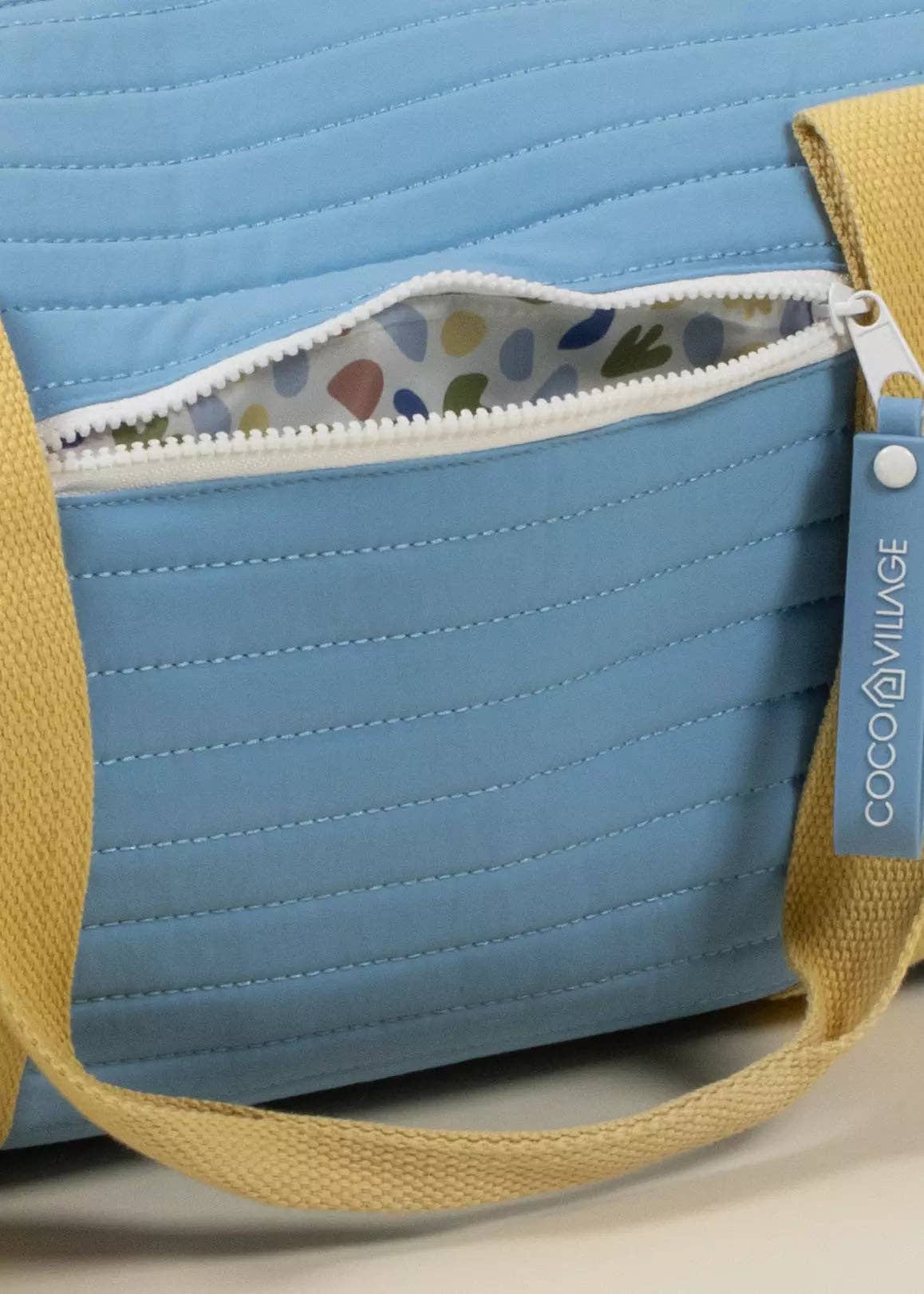 Blue quilted bag with yellow strap and colorful interior lining, featuring a COCO Village tag.