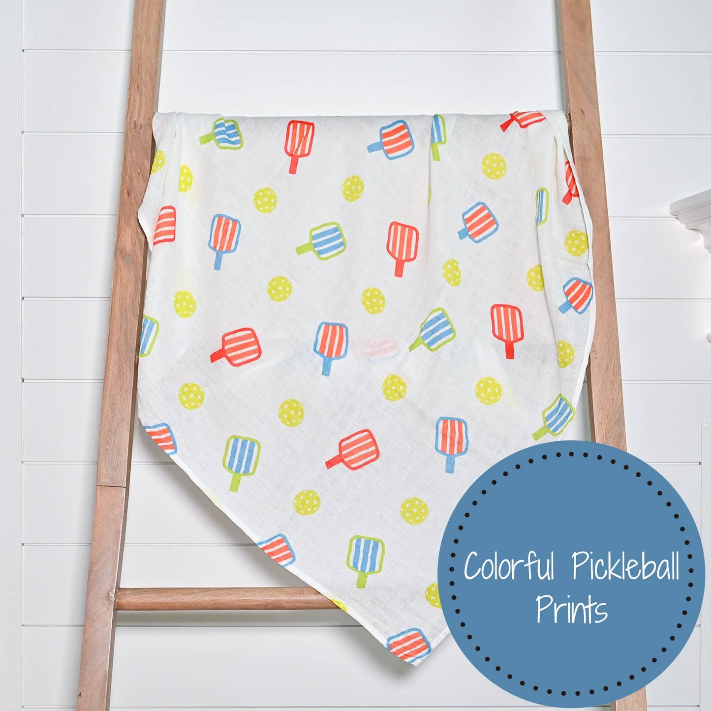 Colorful pickleball patterned blanket draped over a wooden ladder on a white background