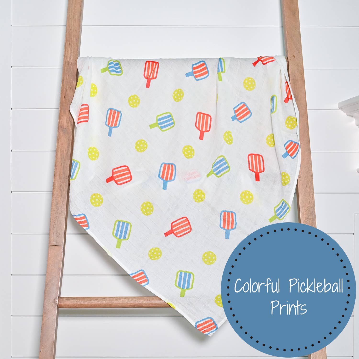 Colorful pickleball patterned blanket draped over a wooden ladder on a white background