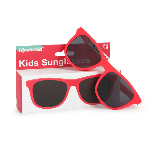 Red kids sunglasses with dark lenses displayed in front of their red and white Hipsterkid retail box on a white background.