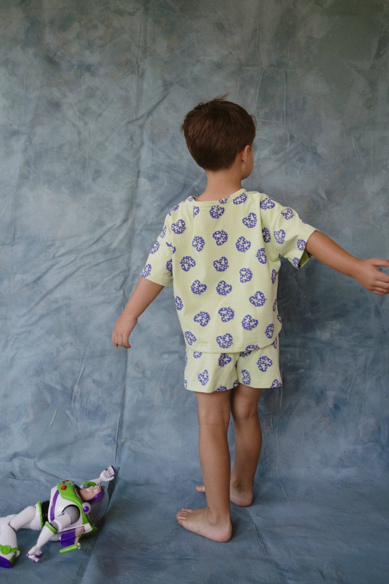 Child in a patterned outfit standing next to a toy on a gray background