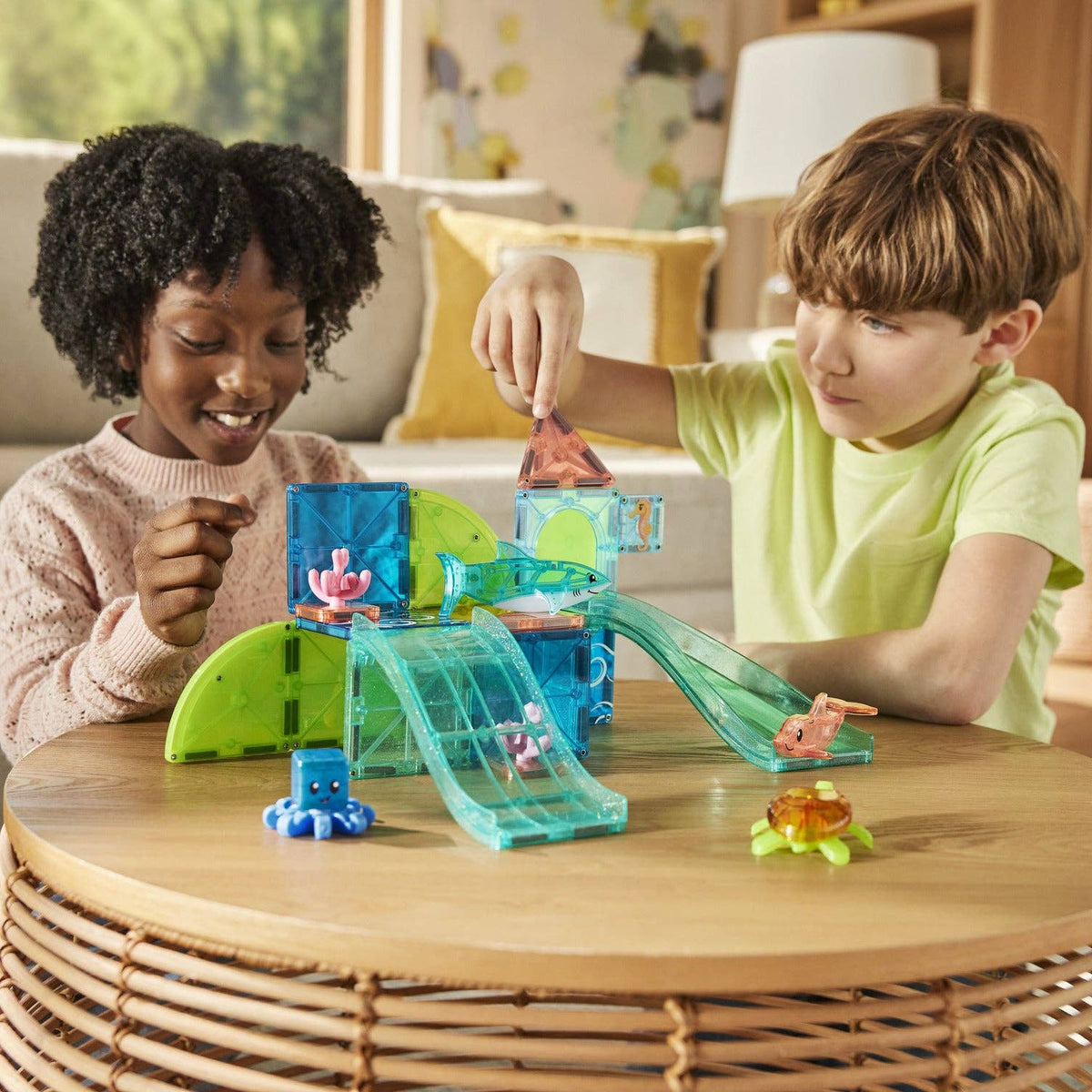 Two children playing with a toy set on a wooden table in a living room.