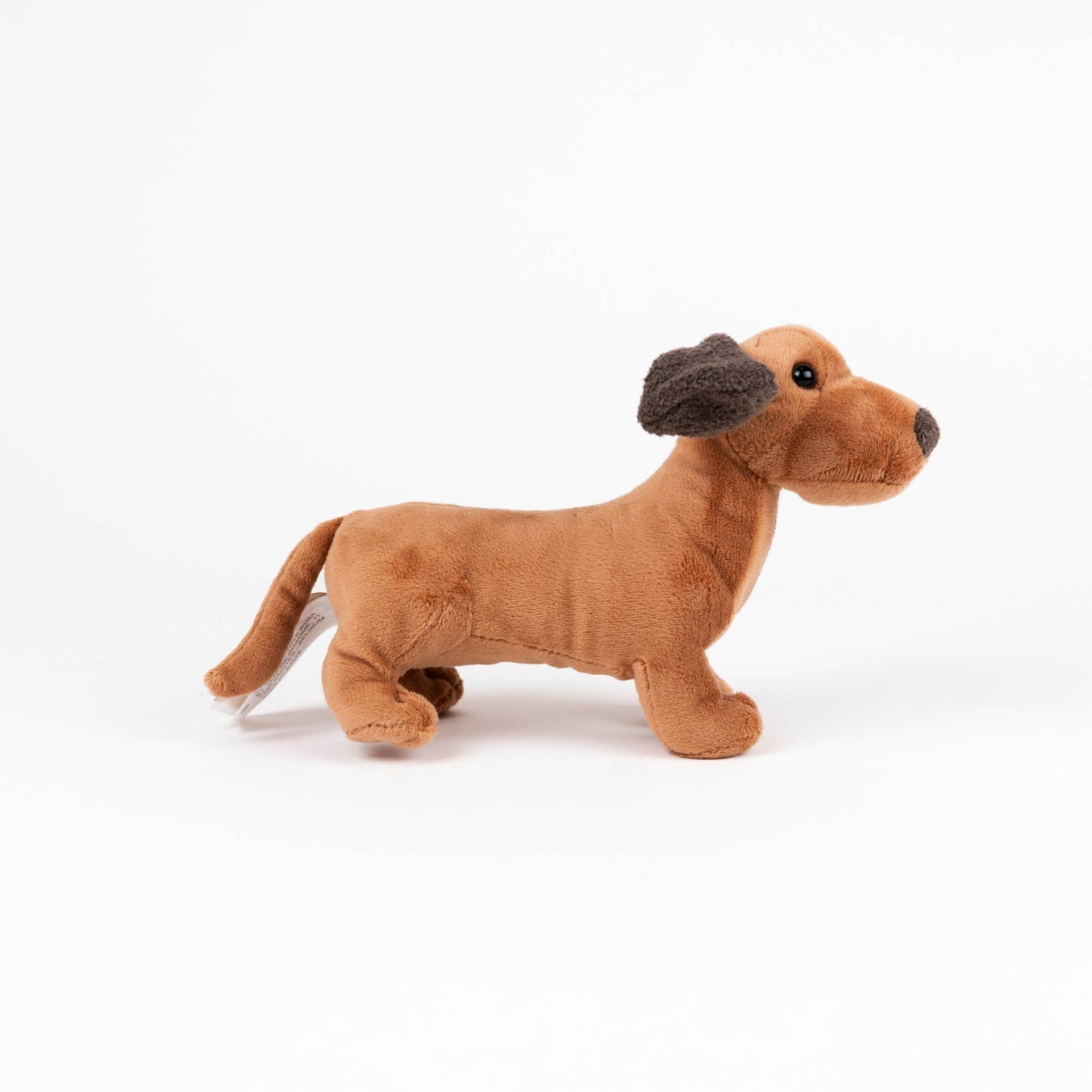 A plush dachshund toy dog in a warm tan-brown color with dark brown ears, standing in profile against a clean white background.