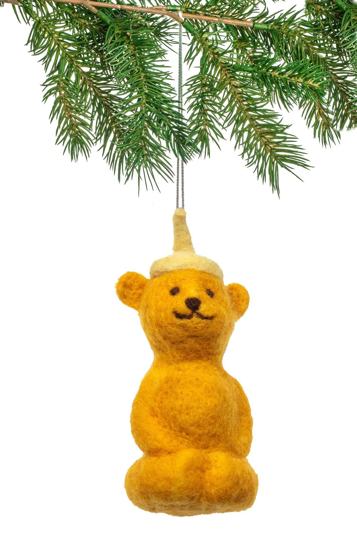 A golden-yellow felt honey bear Christmas ornament hanging from a green pine branch against a white background.