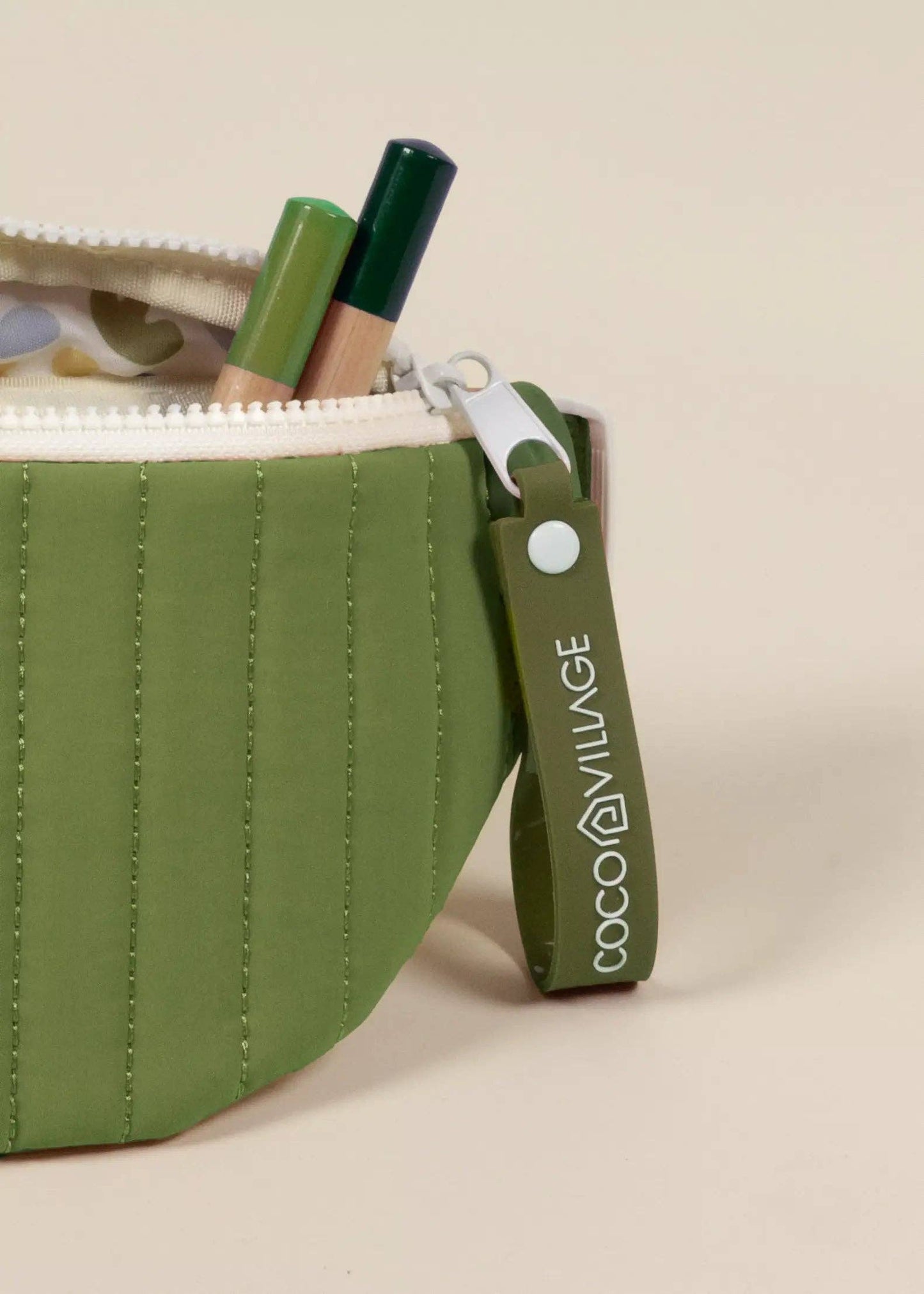 Green pouch with cosmetic items and visible brand logo on a beige background