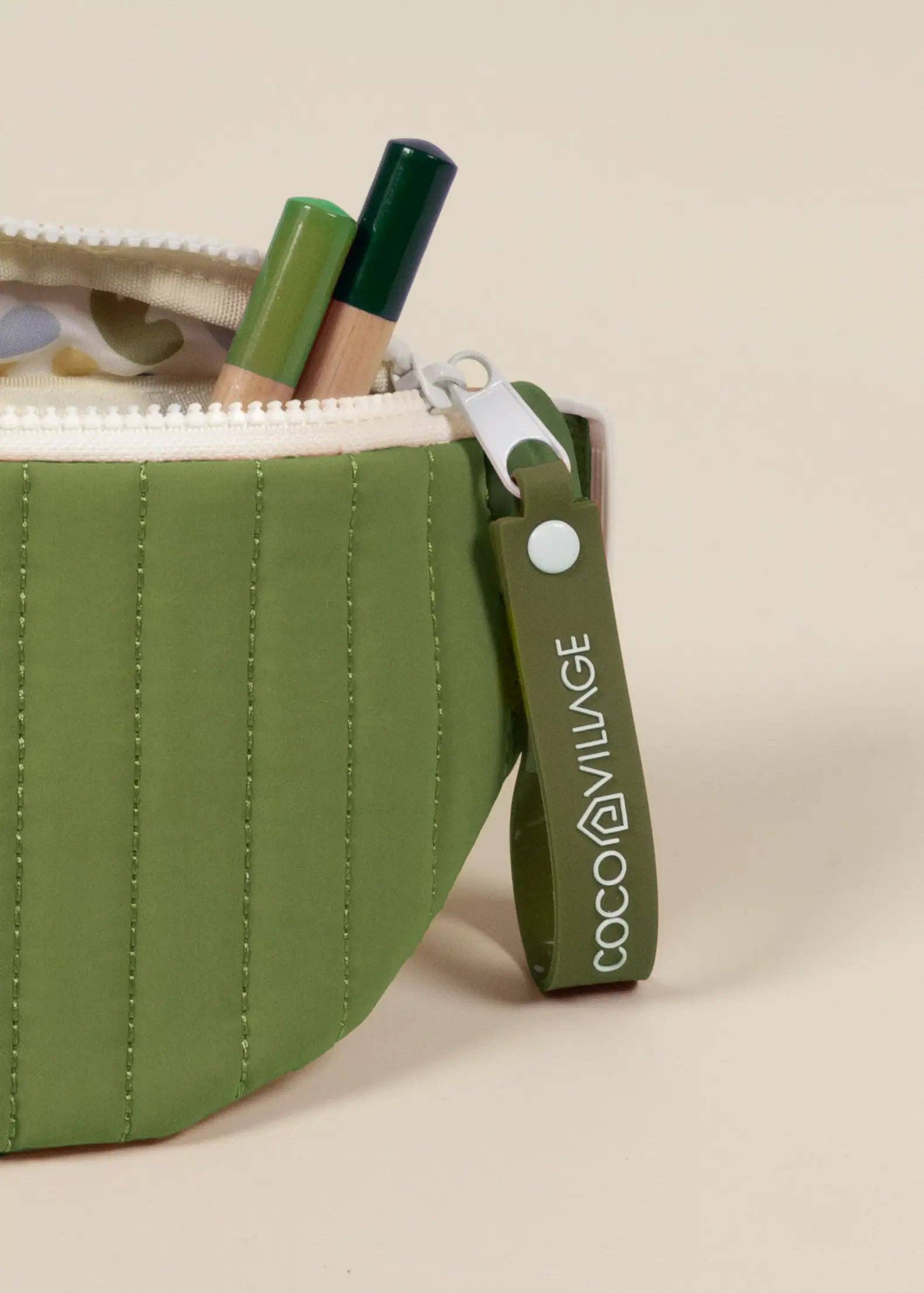 Green pouch with cosmetic items and visible brand logo on a beige background