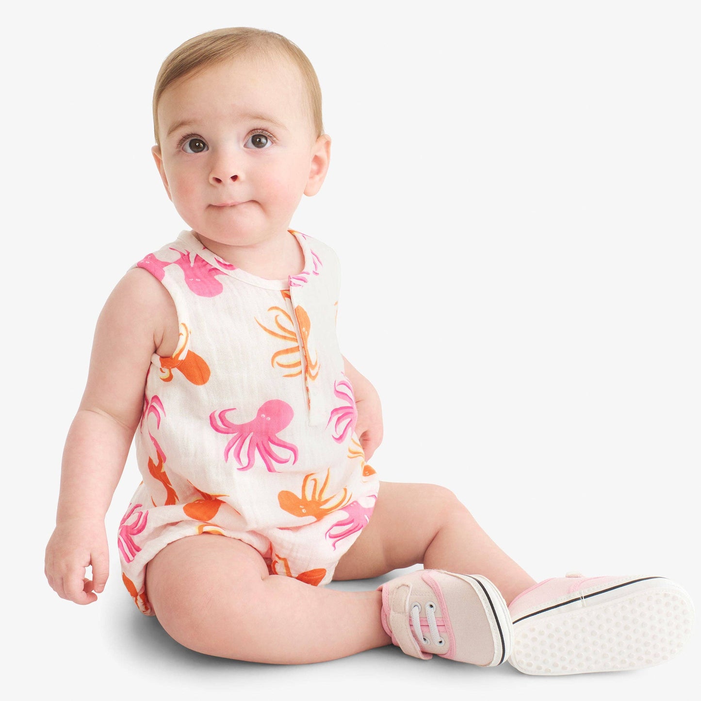 Baby wearing a colorful onesie with pink and orange octopus pattern on a white background