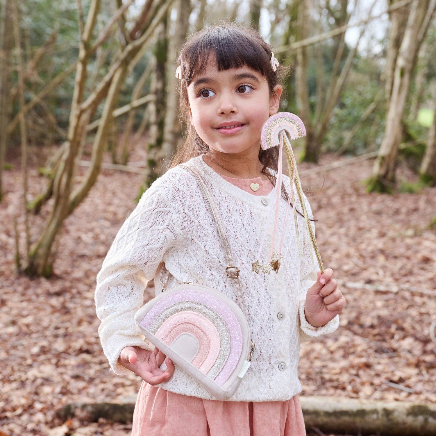 Young girl holding a rainbow-colored bag and wand in a forest setting
