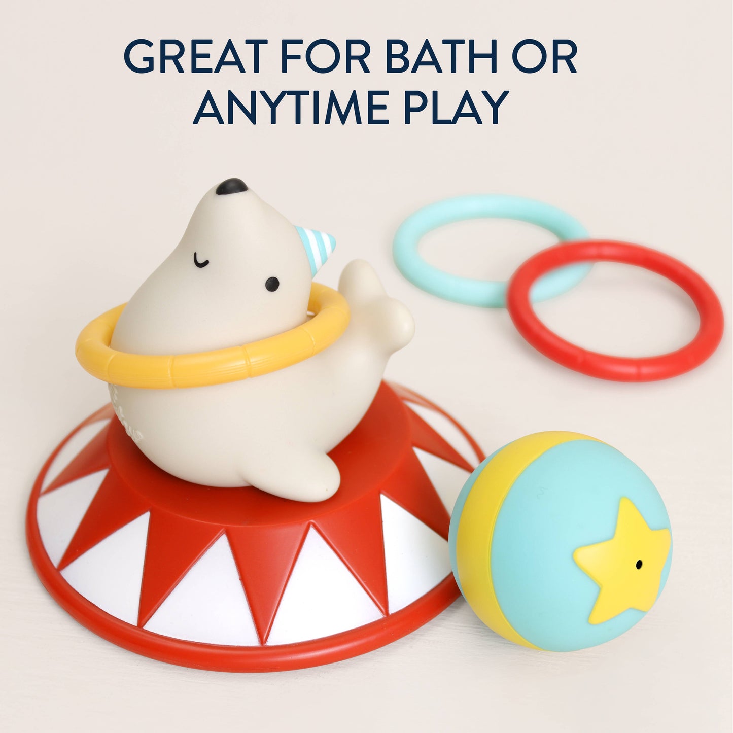 A baby toy set featuring a white seal sitting on a red and white circus-style base, with a yellow ring around its neck, a blue and yellow ball with a yellow star, and two plastic rings in light blue and red. Text at the top reads 'GREAT FOR BATH OR ANYTIME PLAY'.